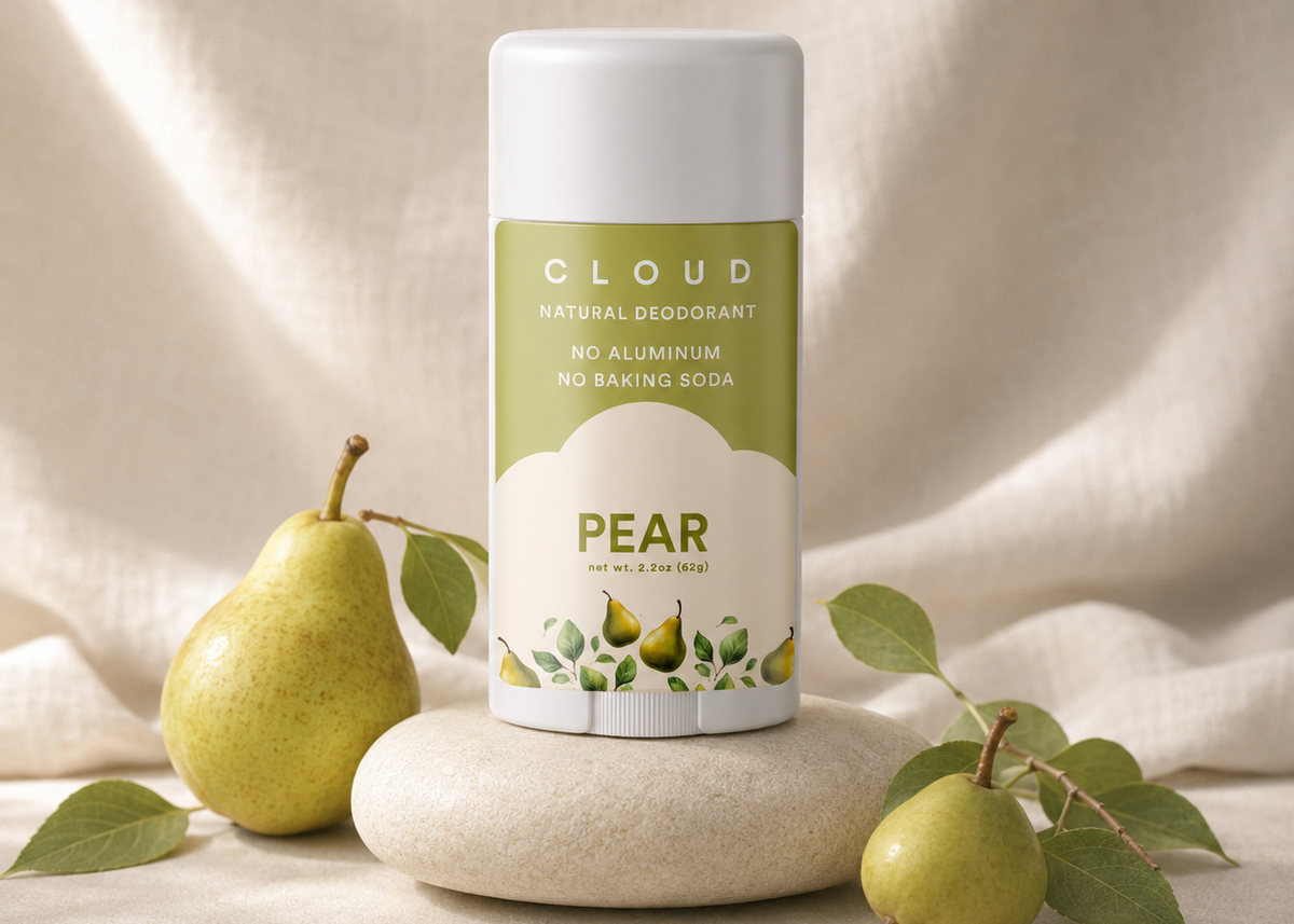 A pear-scented natural deodorant stick by the brand CLOUD, displayed on a stone pedestal with fresh pears and leaves against a draped cream fabric background.